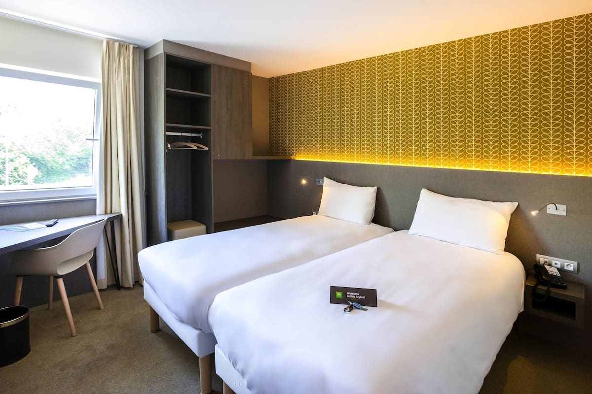 Ein Hotelzimmer mit zwei Betten, einem Schreibtisch, einem Kleiderschrank und einer Wand mit Muster.