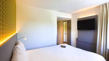 Habitación de hotel con cama, televisor montado en la pared y puerta que da a un pasillo.