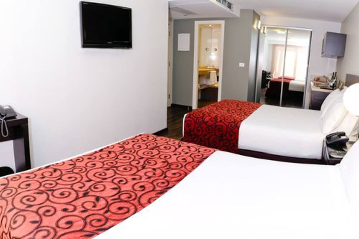 Une chambre d’hôtel avec deux lits, une télévision, un bureau et un miroir.