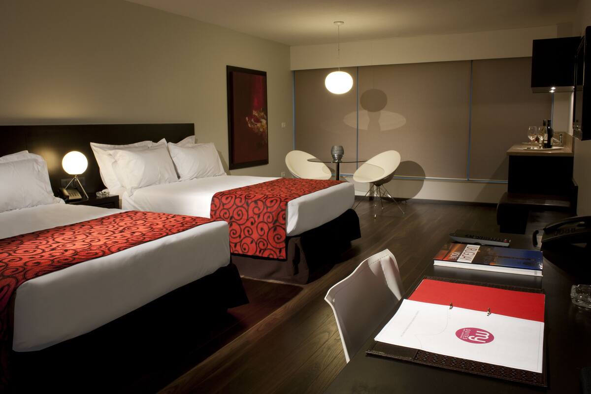 Une chambre d’hôtel avec deux lits, un bureau avec une chaise, une télévision et une grande fenêtre.