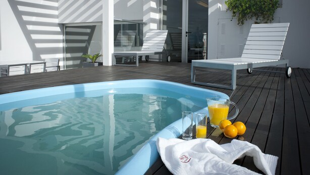 Un área de piscina moderna al aire libre con cerramiento de vidrio, sillas de descanso y una mesa con una toalla y fruta.