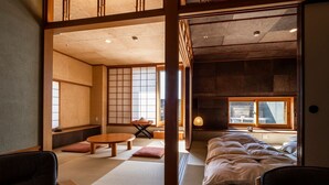 Perinteinen japanilaistyylinen huone, jossa on tatamimatto, matala puinen sänky ja liukuva shoji-paperiovi.
