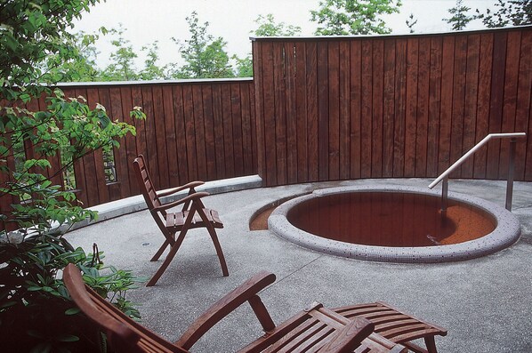 Un patio trasero con cerca de madera, una piscina circular pequeña y dos sillas de madera.