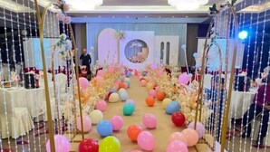 A decorated indoor space with a central aisle lined with colorful balloons and floral arrangements, flanked by tables and chairs. - Ganjiang Hotel (Nanchang)