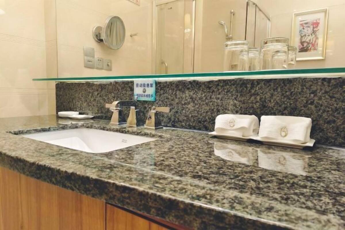 Un baño con encimera de granito, un lavabo, un espejo y un perchero para toallas.
