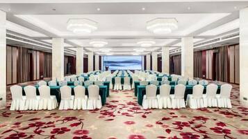 A conference room with rows of tables and chairs, a carpet with a floral pattern, and a view of the sky through a window.