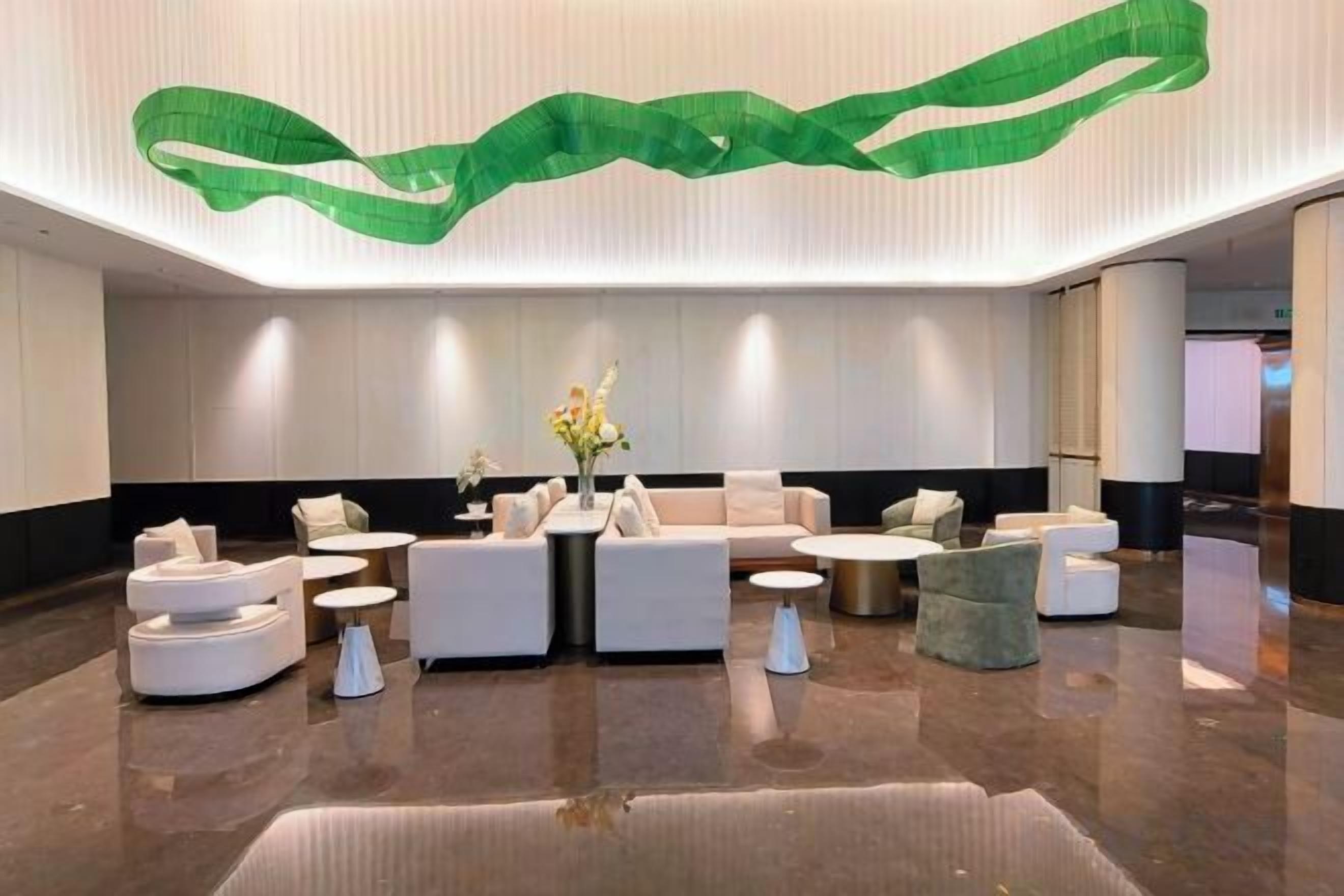 A modern lobby with a seating area, a vase with flowers, and a green ribbon decoration on the ceiling. - Ganjiang Hotel (Nanchang)