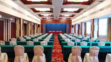 A conference room with rows of tables and chairs, a stage at the front, and a red carpet.