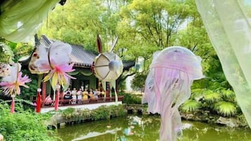 A traditional pavilion with a pond, surrounded by lush greenery.