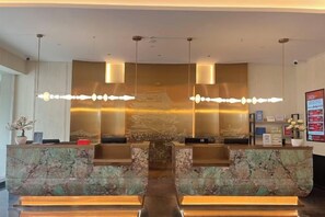 A reception desk with a marble top, two pendant lights, and a wall-mounted screen. - Ganjiang Hotel (Nanchang)