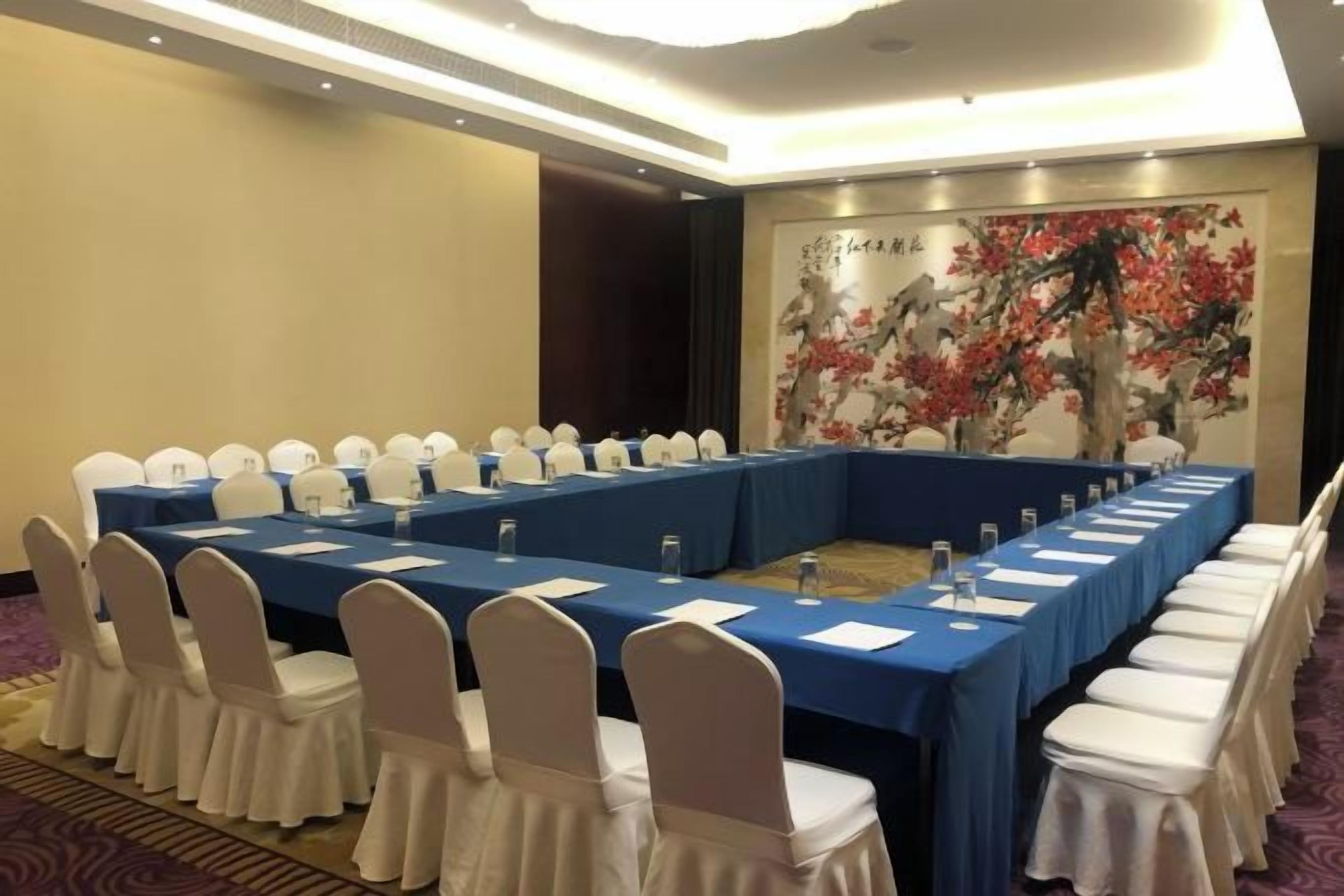 Un salón de conferencias con una larga mesa, sillas blancas y un mantel azul.