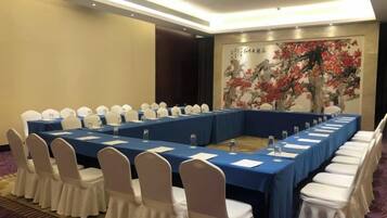 Un salón de conferencias con una larga mesa, sillas blancas y un mantel azul.