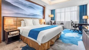 Habitación de hotel con una cama grande, un escritorio, una silla, una lámpara y vistas al exterior.