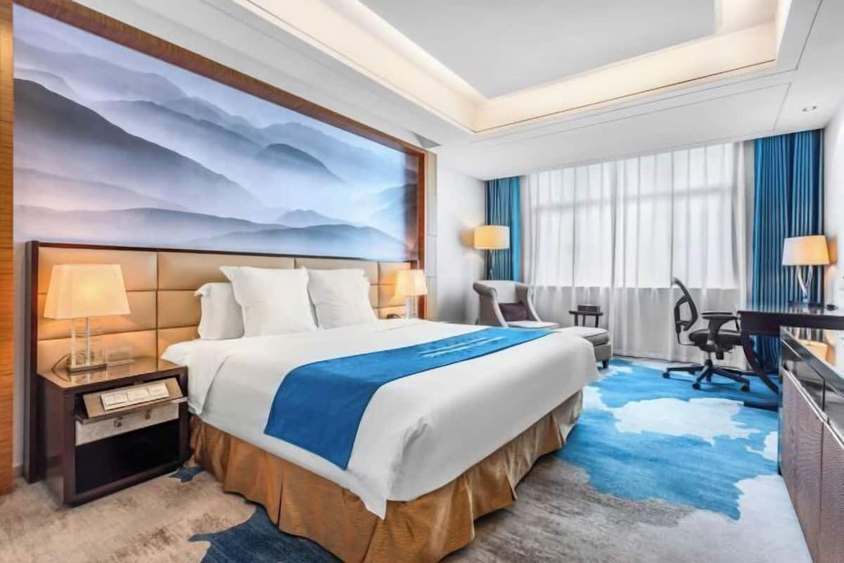 A hotel room with a large bed, a desk, a chair, a lamp, and a view of the outdoors.