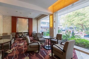 Un vestíbulo de hotel con arreglos de asientos, un ventanal que ofrece vistas al exterior y una alfombra estampada.