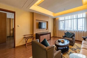 A hotel room with a flat-screen TV mounted on the wall, a sofa, a coffee table, and a large window providing natural light. - Ganjiang Hotel (Nanchang)