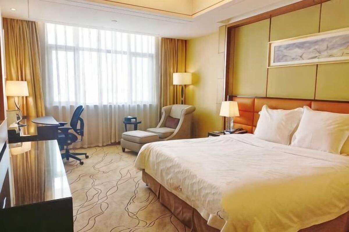 A hotel room with a bed, desk, chair, and lamps.
