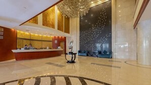A hotel lobby with a reception desk, a large decorative wall, and a patterned floor. - Ganjiang Hotel (Nanchang)