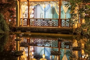 A traditional Chinese-style building with a wooden balcony over a reflective water surface, surrounded by foliage. - Ganjiang Hotel (Nanchang)