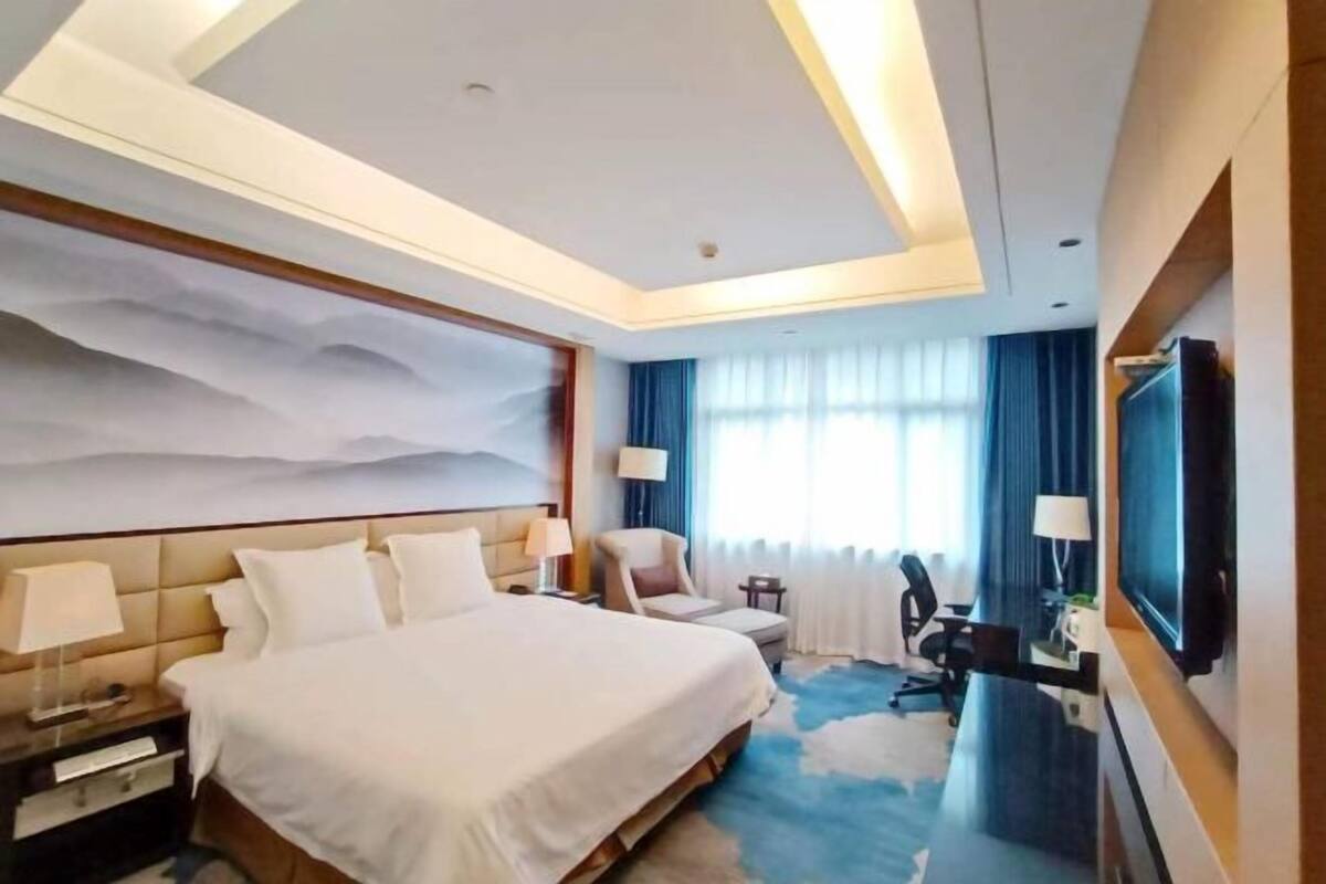 A hotel room with a large bed, a desk, a chair, a TV, and a wall-mounted TV.
