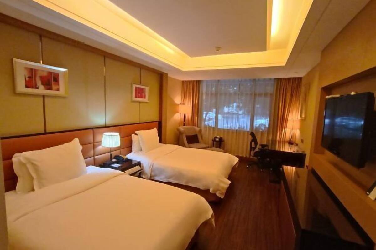 A hotel room with two beds, a TV, a desk, and a chair.
