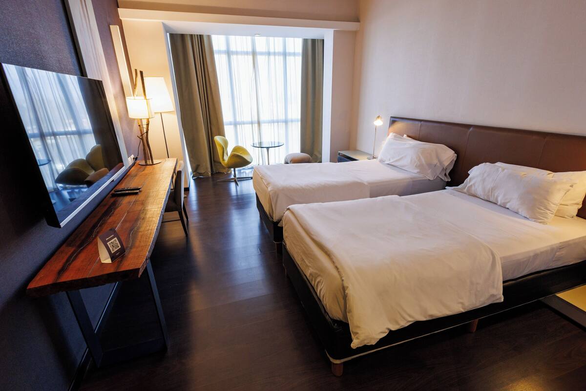 Quarto de hotel com duas camas, televisão, secretária e uma cadeira.