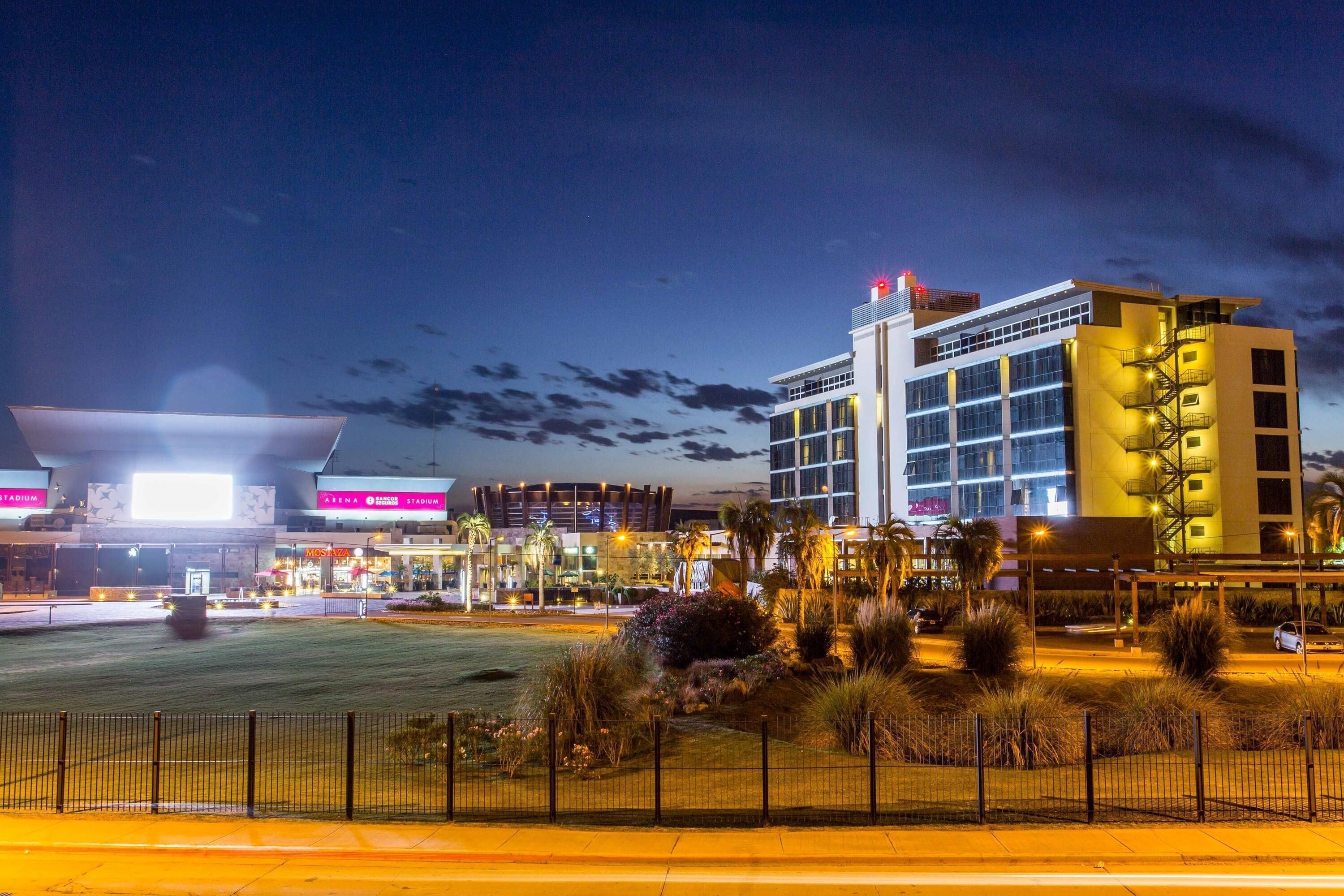 A modern hotel with a prominent entrance, a well-lit parking area, and a landscaped courtyard.