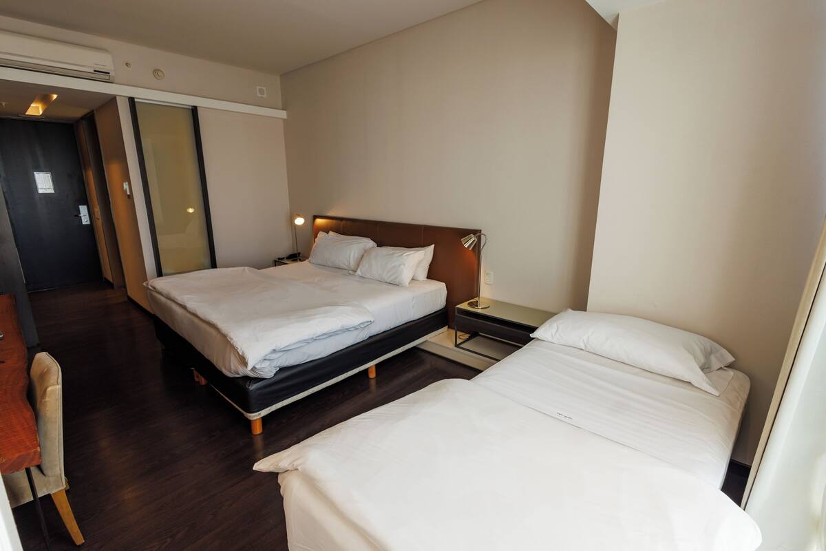 Quarto de hotel com duas camas, uma escrivaninha e uma cadeira.