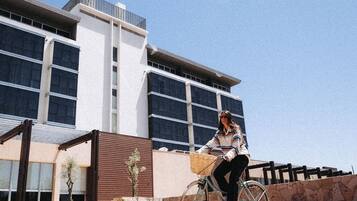 Una persona montando en bicicleta frente a un edificio moderno con ventanas amplias y un muro de piedra.