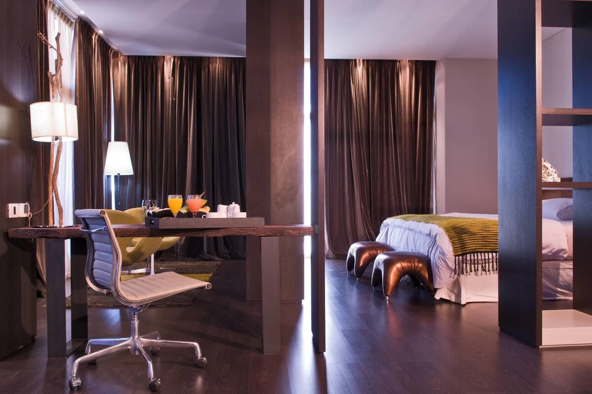 Quarto de hotel moderno com escrivaninha, cadeira e cama com cabeceira.