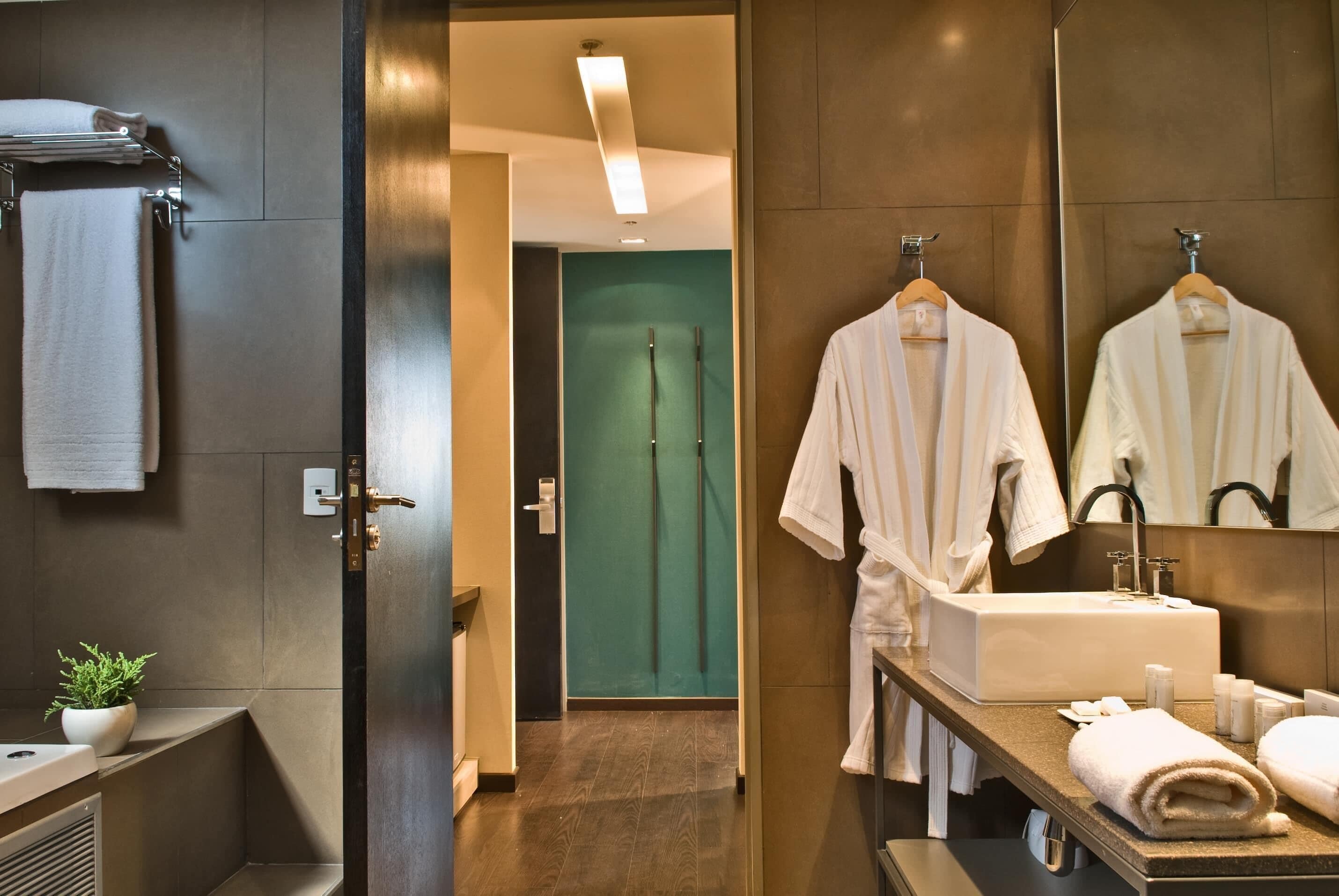 A modern bathroom with a large mirror, a sink, and two white robes hanging on hooks.