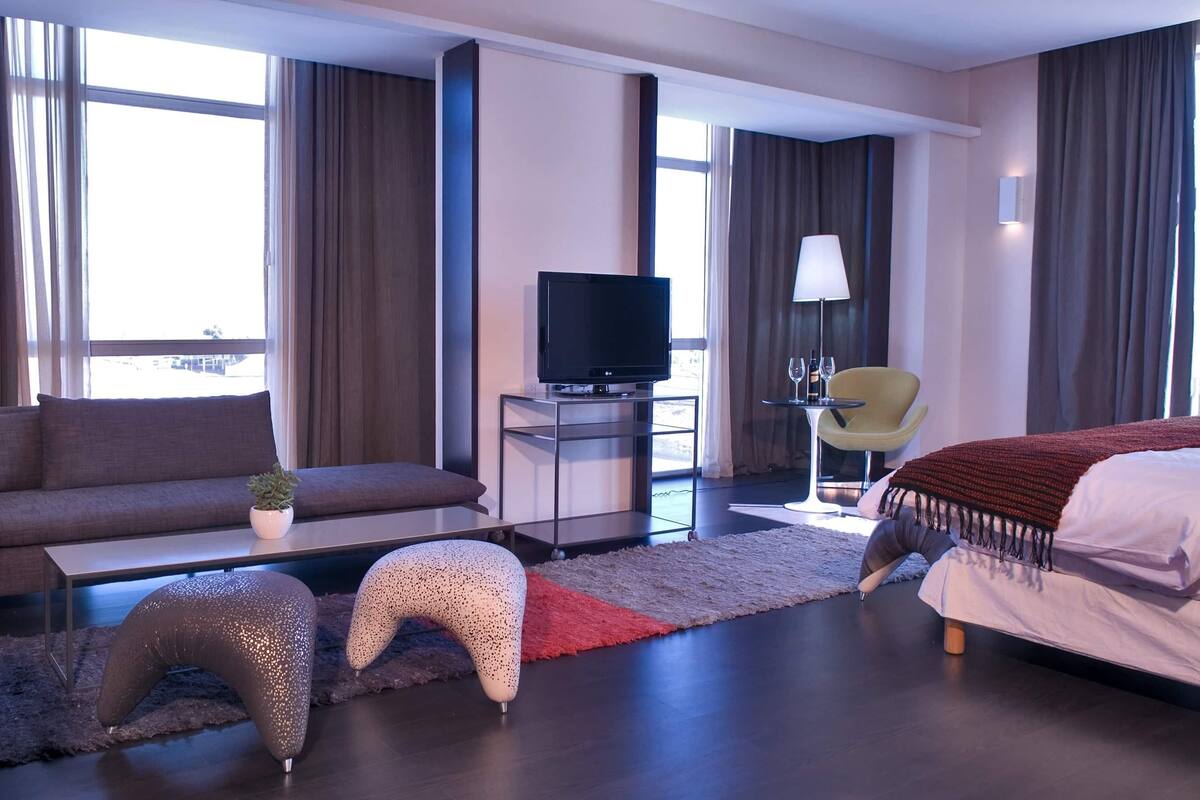 Quarto de hotel moderno com sofá, televisão, mesa pequena, cadeira e cama.