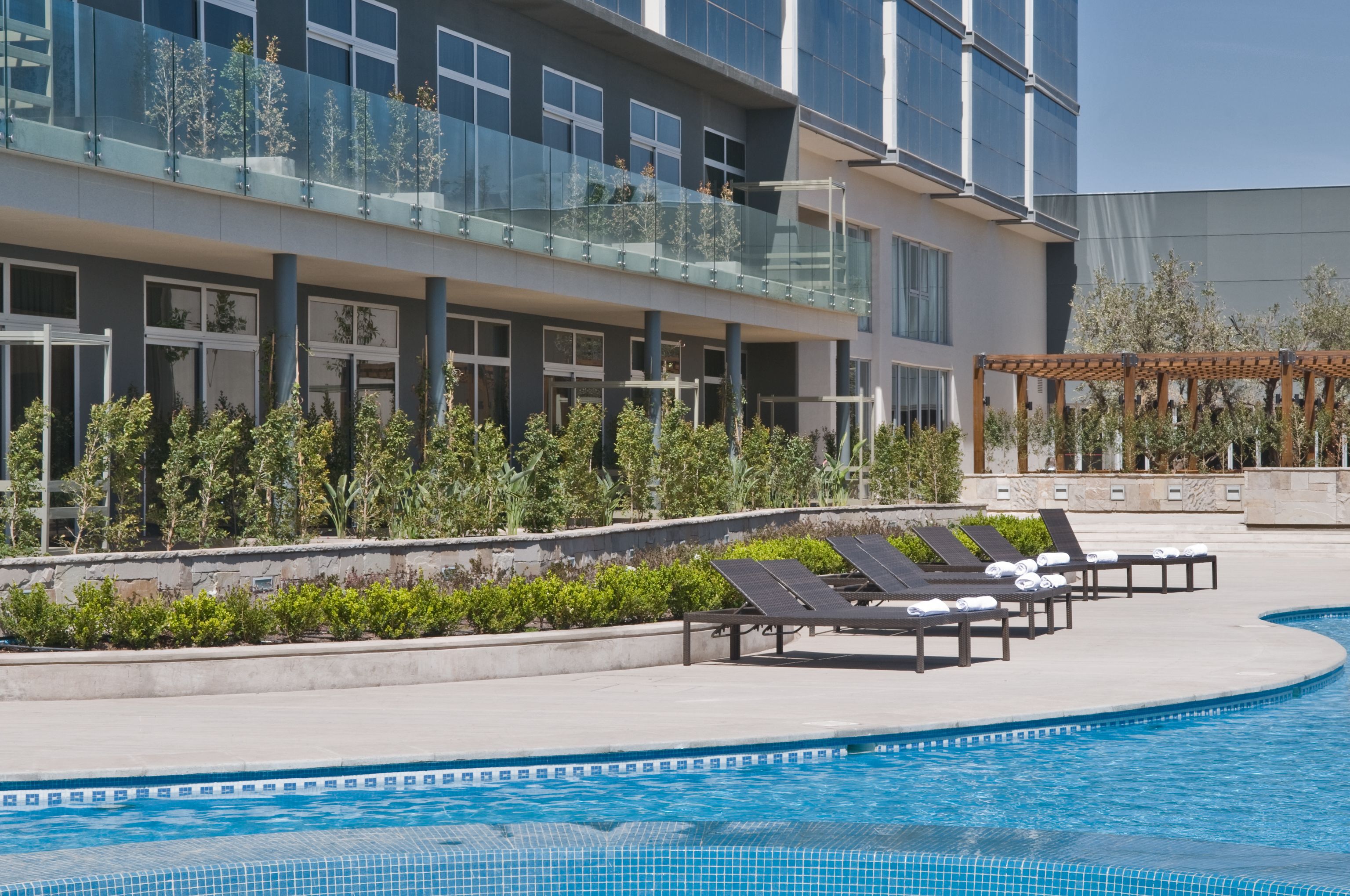 A modern hotel with a swimming pool, sun loungers, and a glass balustrade overlooking the pool.