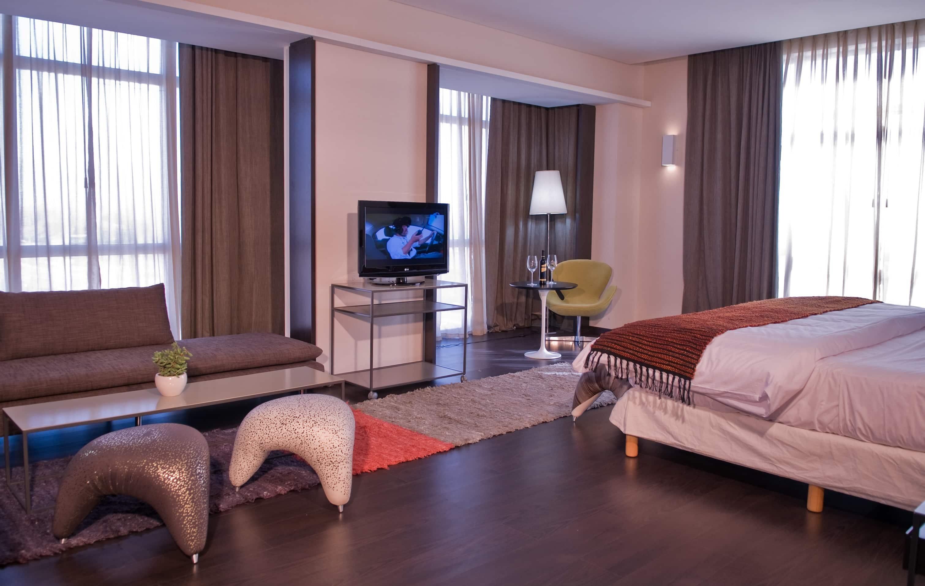 A hotel room with a bed, sofa, TV, small table, and a chair.