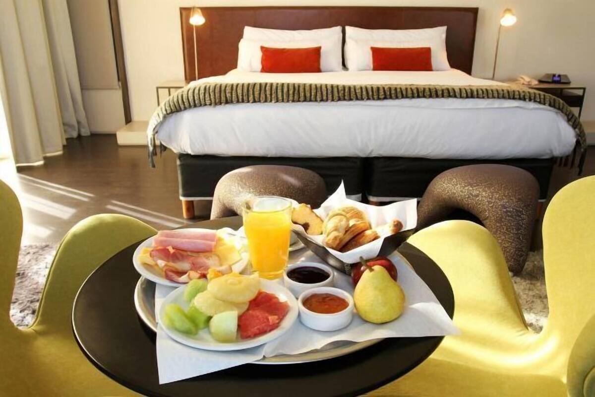 Ein Hotelzimmer mit Bett, Frühstückswagen mit Obst, Gebäck und Getränken sowie einem Sessel.