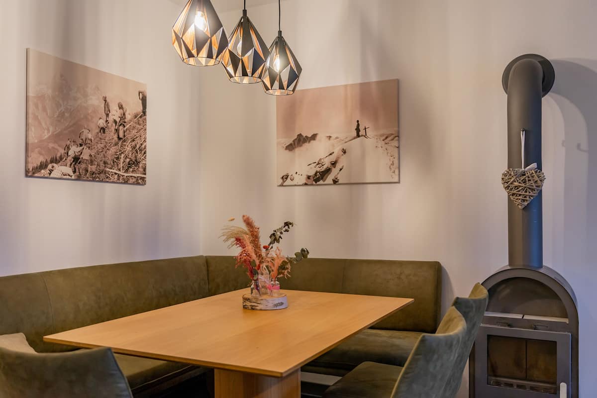 Ein gemütlicher Essbereich mit Holztisch, grün gepolsterten Sitzgelegenheiten, Pendelleuchten und Wandbildern.