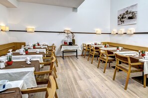 Un restaurant avec des tables et des chaises en bois, des nappes blanches et des plantes en pot.