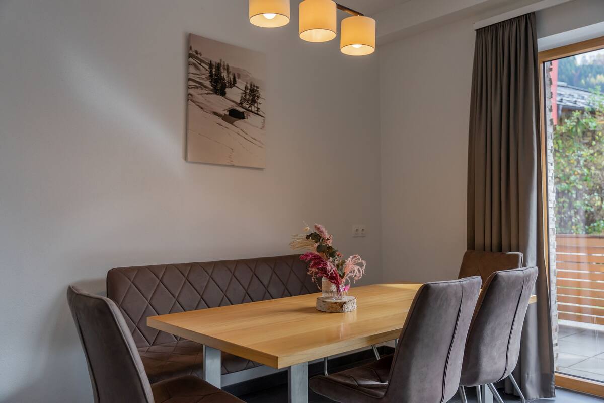 Ein Essbereich mit Holztisch, gepolsterten Sitzbänken und einer Blumenvase.