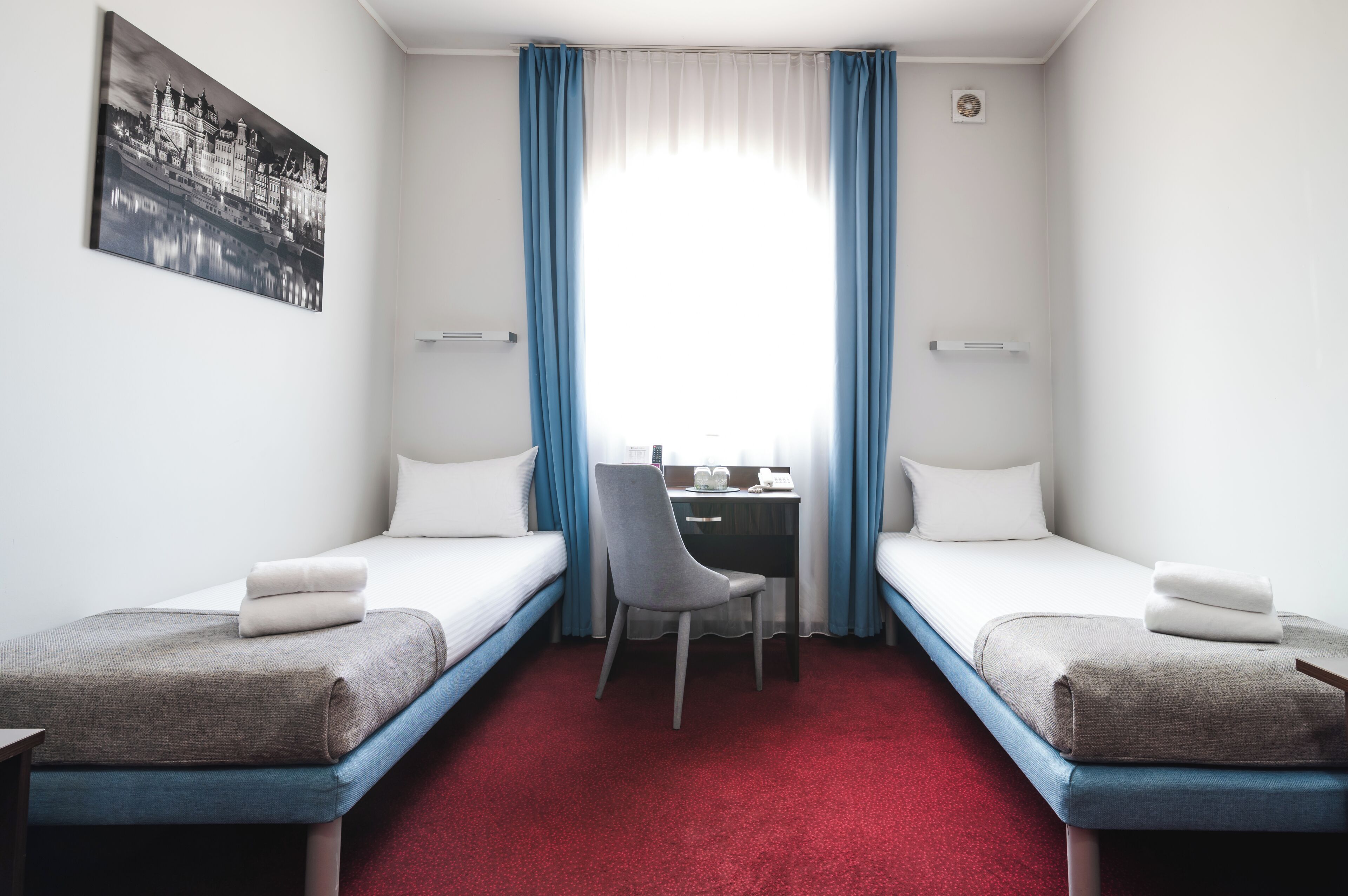 Una habitación de hotel con dos camas individuales, un escritorio, una silla y un amplio ventanal con cortinas.