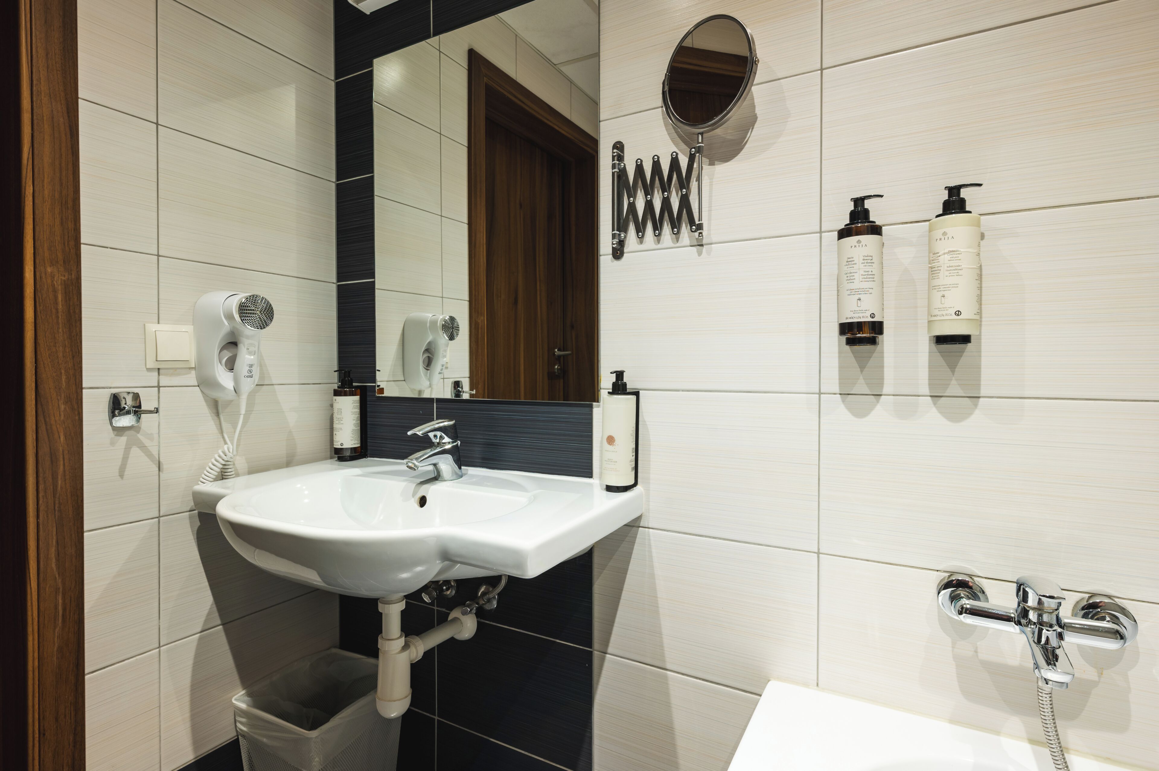 Un bagno con lavandino bianco, uno specchio, un asciugacapelli, un portascopevoli e una doccia.