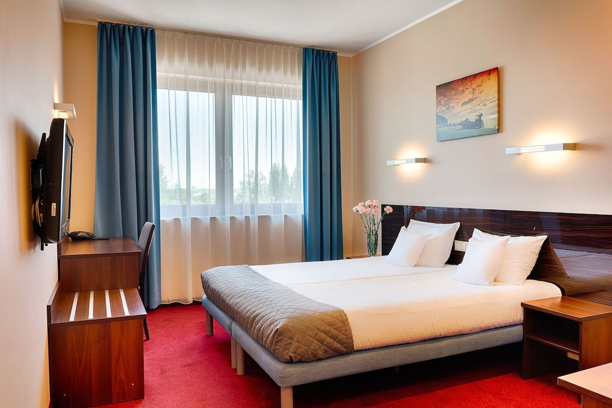 Una habitación de hotel con una cama grande, un escritorio, una silla, un televisor y un cuadro en la pared.