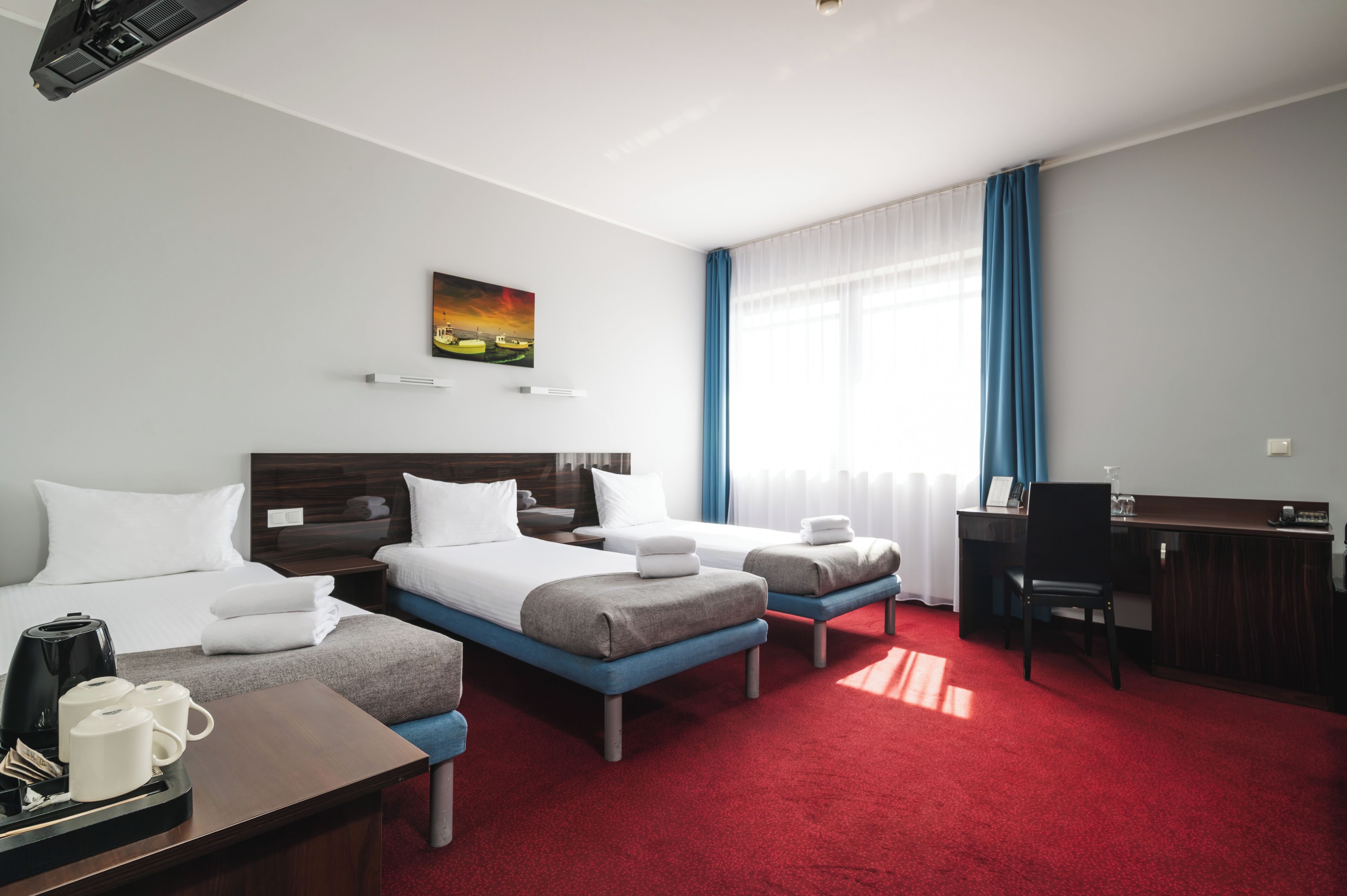 Habitación de hotel con dos camas, un escritorio, una silla, una cafetera y un cuadro en la pared.