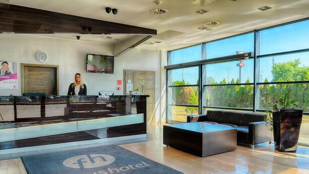 A modern hotel lobby with a reception desk, seating area, and large windows offering a view of greenery. - Hotel Focus Gdansk (Gdansk)