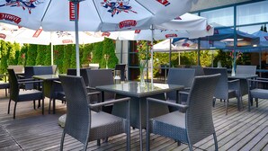 An outdoor patio with wicker furniture and white umbrellas with logos. - Hotel Focus Gdansk (Gdansk)