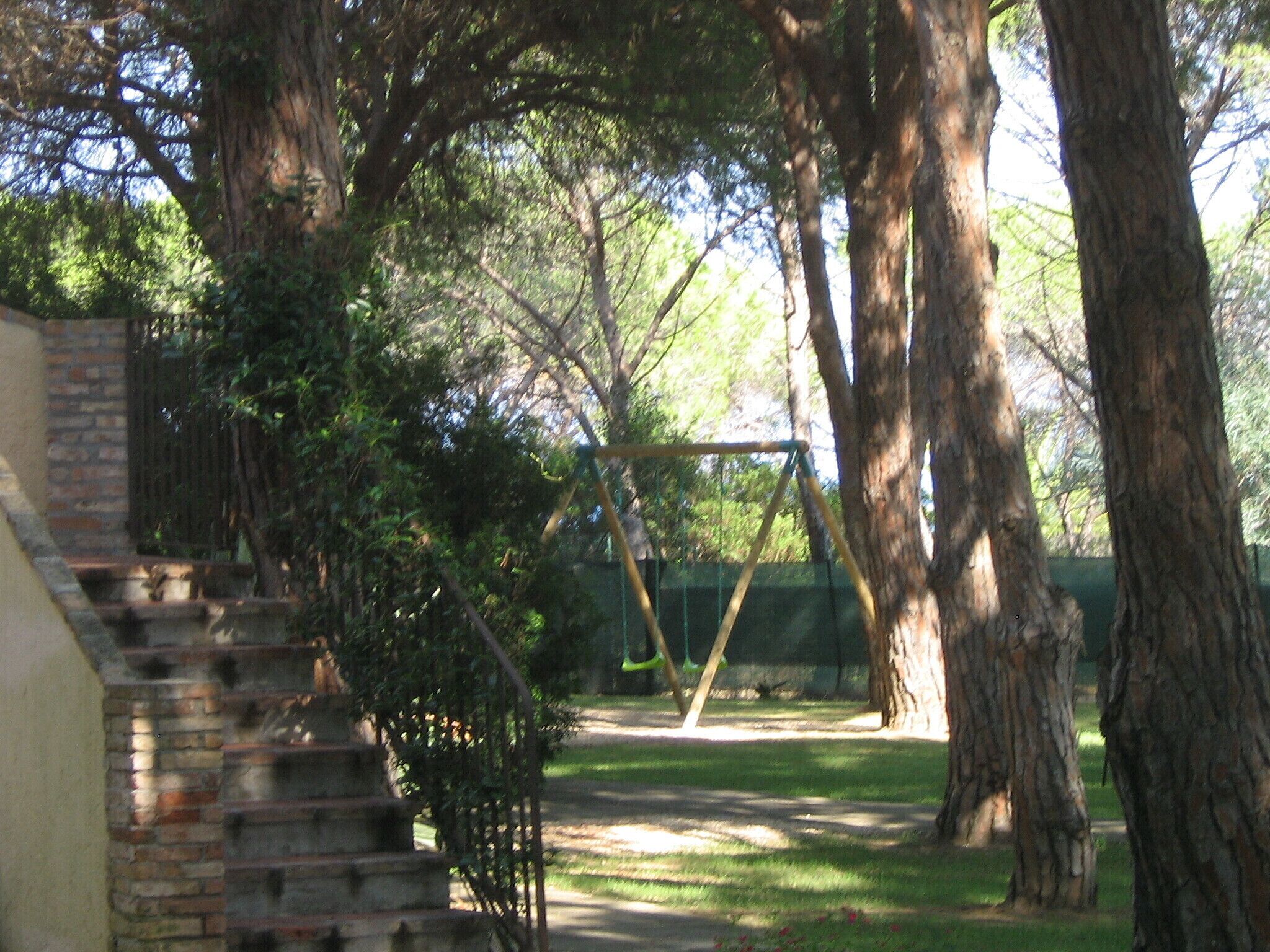Un escalier en briques mène à une zone abritée, entourée d’arbres et agrémentée d’une balançoire, le tout dans un cadre qui rappelle un parc.