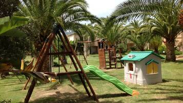Children can play on the swing set and slide in this outdoor play area surrounded by lush greenery.