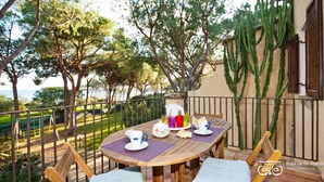 Mesa de madera con tazas y una jarra en un balcón con vistas a un jardín y al mar.