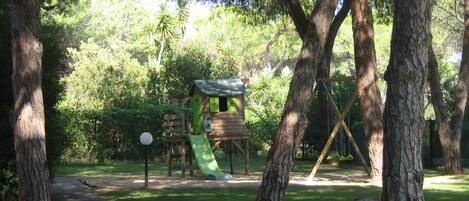 A playground with a slide, swings, and a climbing structure surrounded by trees.
