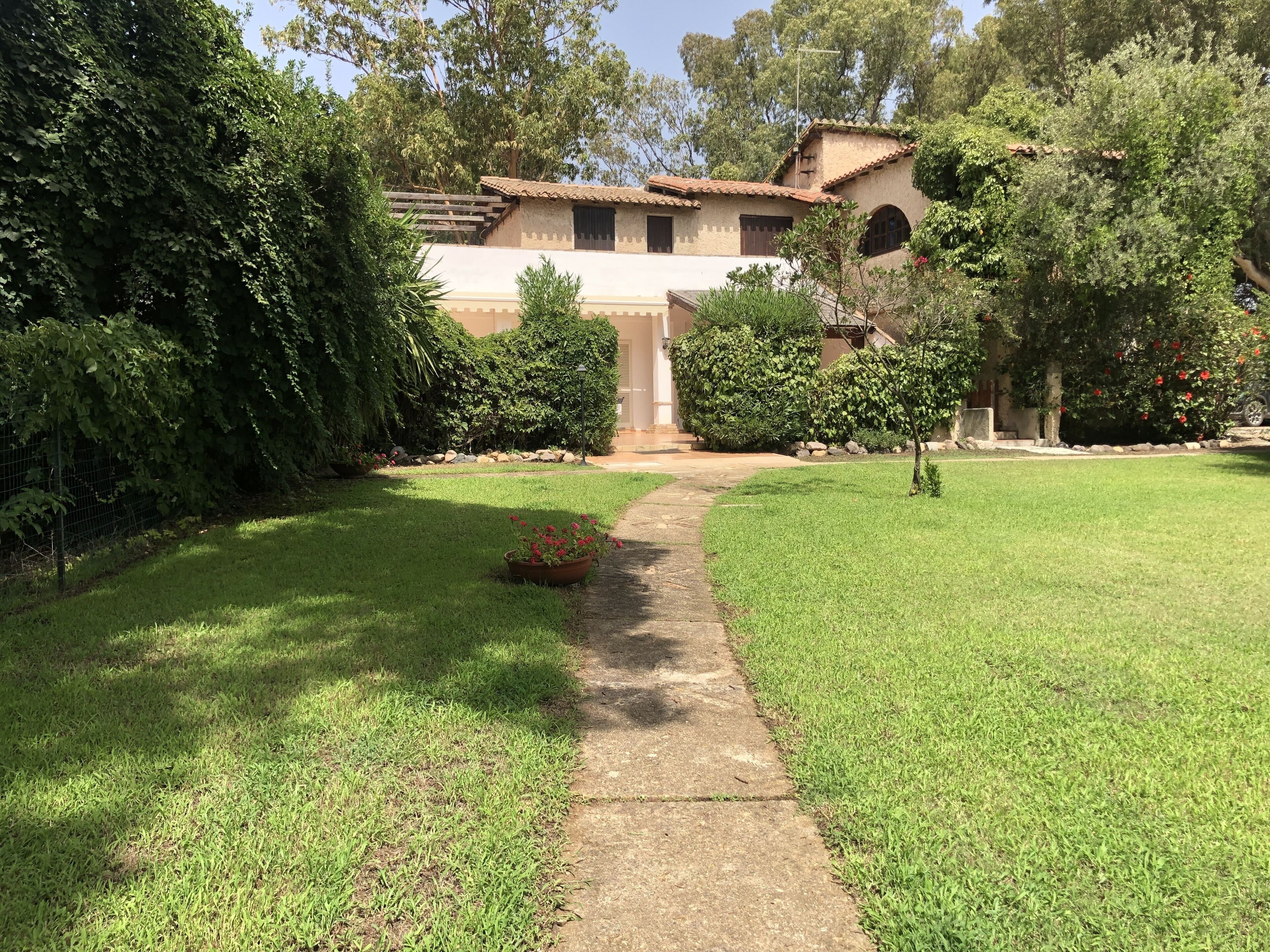 Una casa con un sendero pavimentado que conduce a la entrada, rodeada de césped cuidado y diversos arbustos.