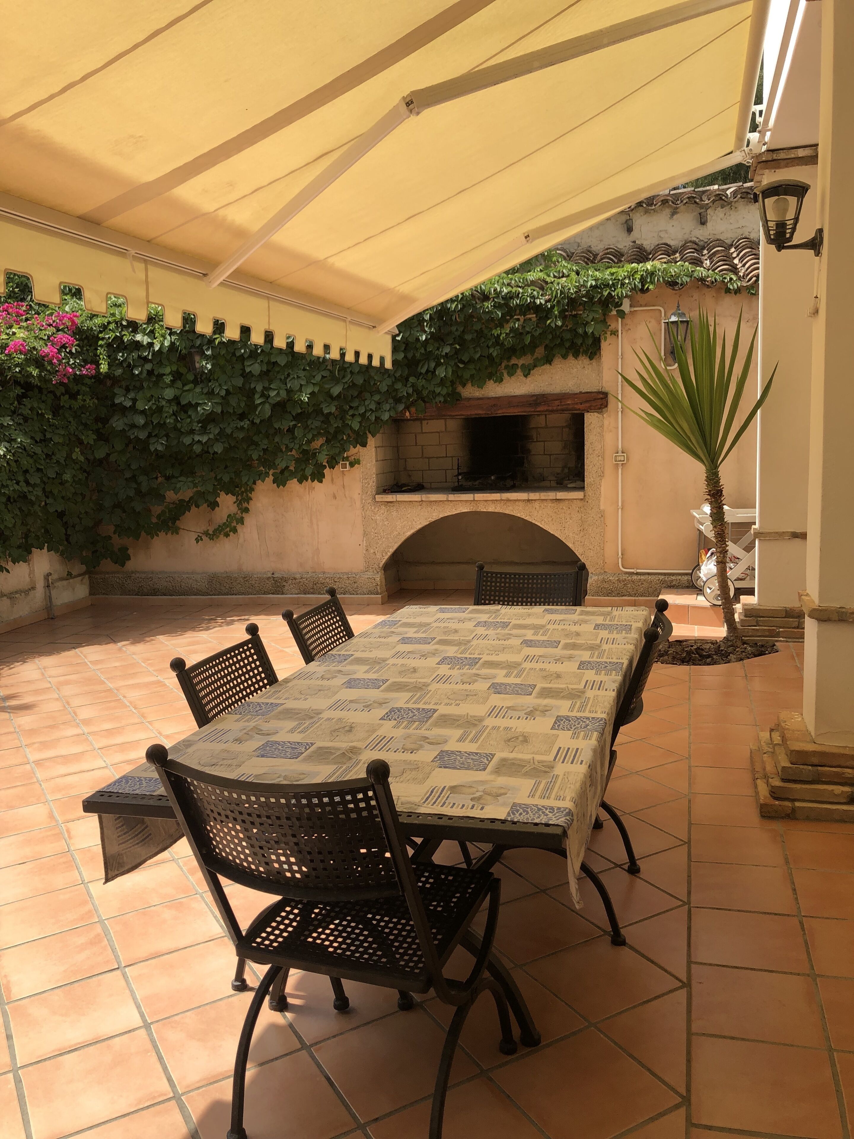 An outdoor patio with a table and chairs, a brick oven, and a pergola with climbing plants.